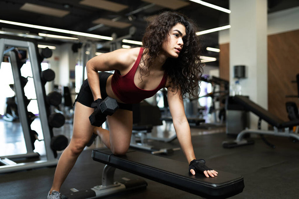 Mulher latina bonita fazendo um exercício de haltere em um banco de sentar-se no centro de fitness - Foto, Imagem
