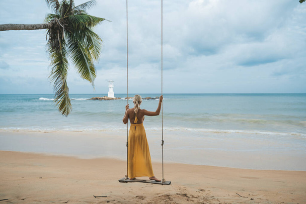 Young woman in yellow dress swing on swing on the beach in Kao Lak, Thailand - Foto, afbeelding