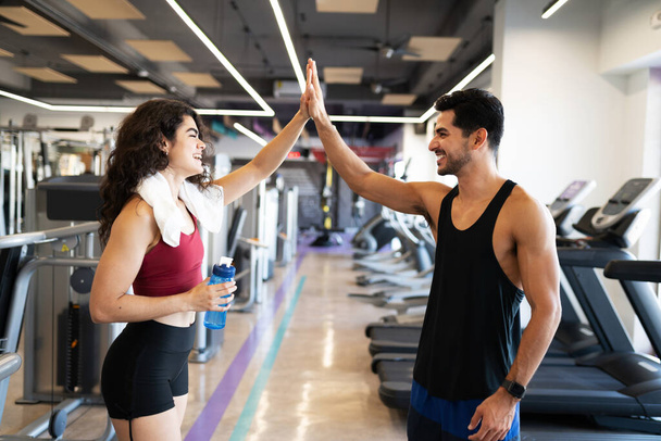 Latijnse jonge vrouw en latino fit man lachen en vieren het bereiken van hun fitness doelen in de sportschool - Foto, afbeelding
