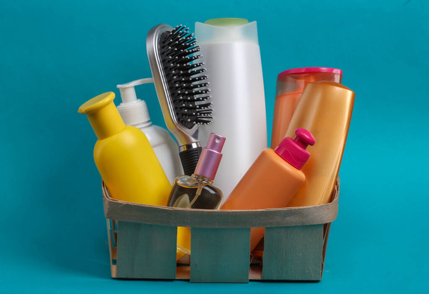 Bottiglie di cosmetici, shampoo, pettine in un cestino di legno su sfondo blu. Prodotti di bellezza - Foto, immagini