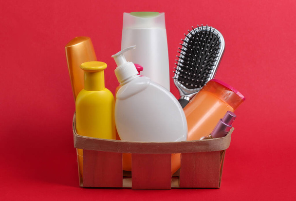 Bottiglie di cosmetici, shampoo, spazzola per capelli in un cesto di legno su sfondo rosso. Prodotti di bellezza - Foto, immagini