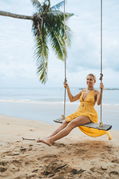 Young woman in yellow dress swing on swing on the beach in Kao Lak, Thailand - Фото, зображення