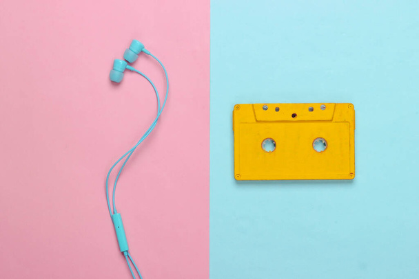 Retro-Audio-Kassette mit Kopfhörer auf rosa blauem Hintergrund. 80er Jahre. Ansicht von oben. Minimalismus. - Foto, Bild