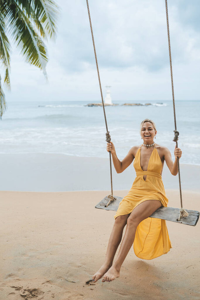 Young woman in yellow dress swing on swing on the beach in Kao Lak, Thailand - Zdjęcie, obraz