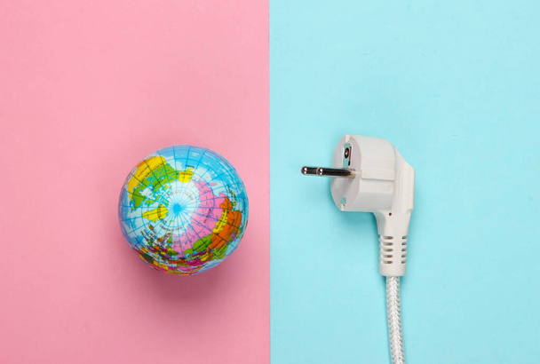 Koncepcja ekologiczna. Oszczędzanie energii Ocal planetę. Globus z wtyczką elektryczną na niebiesko-różowym pastelowym tle. Widok z góry - Zdjęcie, obraz
