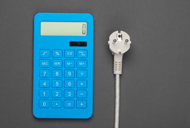 Taschenrechner mit Netzstecker auf grauem Hintergrund. Berechnung der Energieverbrauchskosten. Ansicht von oben - Foto, Bild