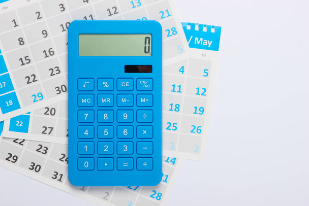 Calcolatrice con i fogli del calendario mensile su sfondo bianco. Calcolo dei pagamenti per l'affitto di alloggi. Vista dall'alto - Foto, immagini