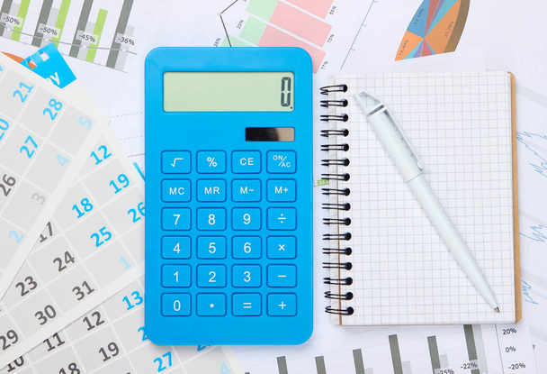 Calculadora con cuaderno, gráficos y gráficos, calendario mensual. Cálculo económico, costos. Negocios y Finanzas - Foto, imagen