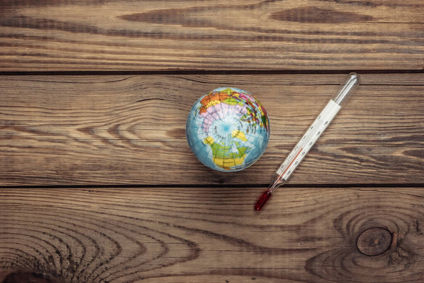 Global warming concept. Globe with thermometer on a wooden background. Top view - Fotografie, Obrázek