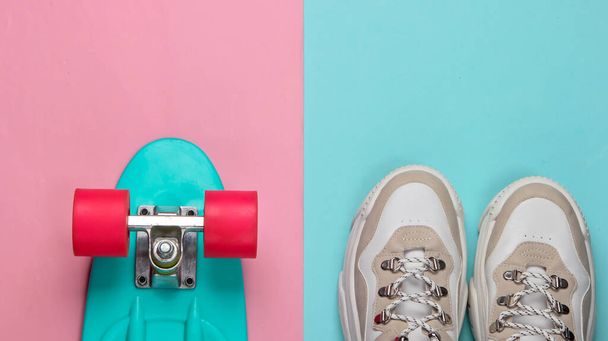 Fashionable sneakers with cruiser board on pink blue pastel background. Youth fun. Top view. Minimalism - Photo, Image