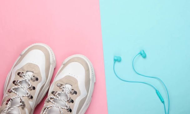 Sneakers alla moda con auricolari su sfondo rosa pastello blu. Vista dall'alto. Minimalismo - Foto, immagini