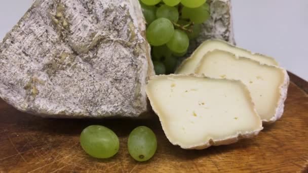 Un plato de surtidos quesos de leche de cabra mohosa en una mesa de madera con uvas verdes - Metraje, vídeo