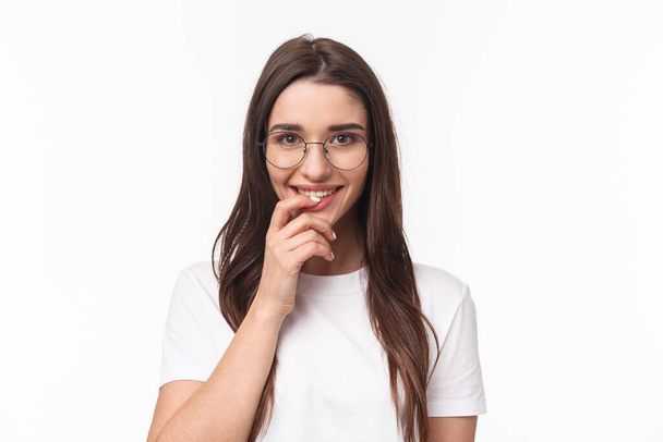 Close-up portrait of excited feminine, cute young woman in glasses, smiling and looking with temptation or desire, touching lip, want try something tasty, standing white background - Photo, Image