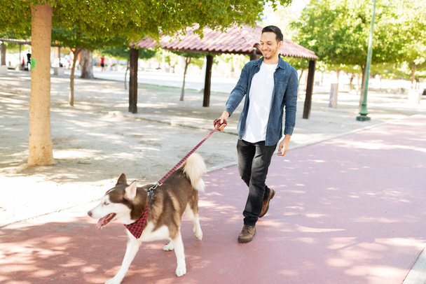 Vista lateral de um belo cão feliz com uma trela andando com seu dono de cão macho na pista de corrida do parque - Foto, Imagem
