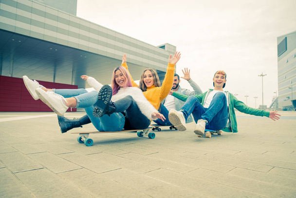 Group of teenagers fooling about at skate park - Happy young friends sitting on skateboard - Group of cheerful friends having fun, concepts about teenage, lifestyle and generation z - Photo, Image