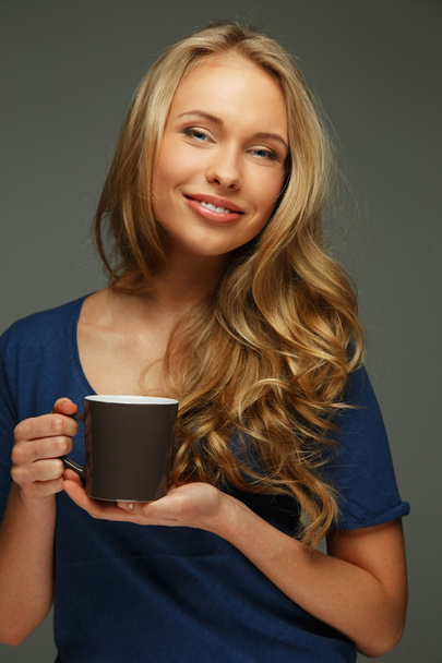 Позитивна молода жінка з довгим волоссям і блакитними очима тримає чашку
 - Фото, зображення