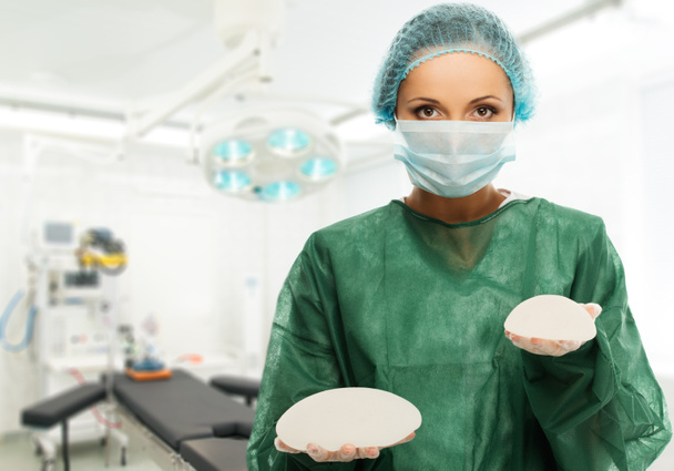 手術室内で異なるサイズのシリコン乳房インプラントを保持している形成外科医女性  - 写真・画像