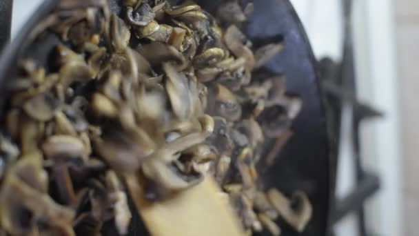 verticale video gebakken champignes in een hete zwarte koekenpan.Roer de gebakken champignons half gaar met een houten spatel. - Video