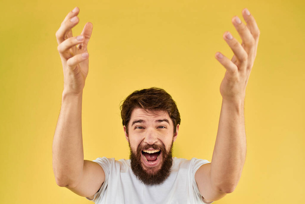 A man in a white t-shirt gestures with his hands lifestyle cropped view yellow background more fun - Foto, Imagen