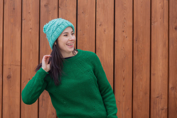 Χαμογελώντας ευρωπαϊκή γυναίκα σε πράσινο πουλόβερ και πράσινο καπέλο σε ξύλινο φόντο - Φωτογραφία, εικόνα
