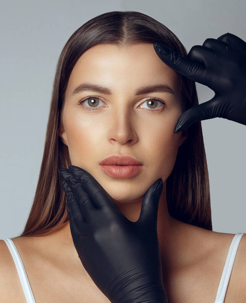 Dermatolog w czarnych rękawiczkach sprawdza twarz kobiety przed operacją plastyczną - Zdjęcie, obraz