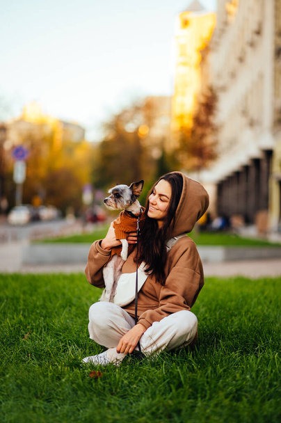 Gelukkige vrouw zittend op een groen grasveld met een hondenras biewer terriër in haar armen, kijkend naar een huisdier met een glimlach op zijn gezicht. glimlachende dame brengt tijd door met een hond. - Foto, afbeelding