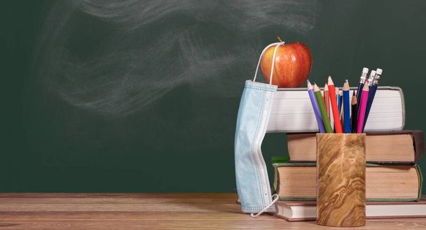 Yüz maskeli elma ve kitap yığınıyla sanal okul arka plan kavramına geri dönelim. - Fotoğraf, Görsel