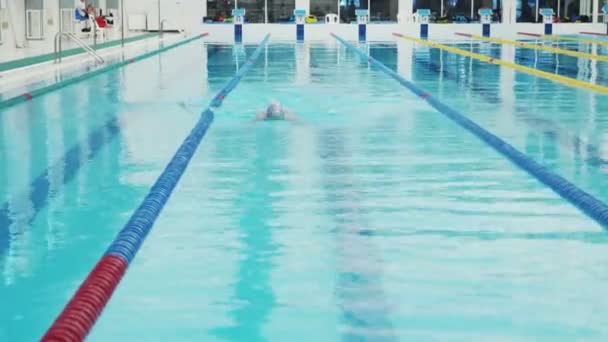 Professionele zwemmer nauwelijks uit te werken in het overdekte zwembad zwemmen over de baan. - Video