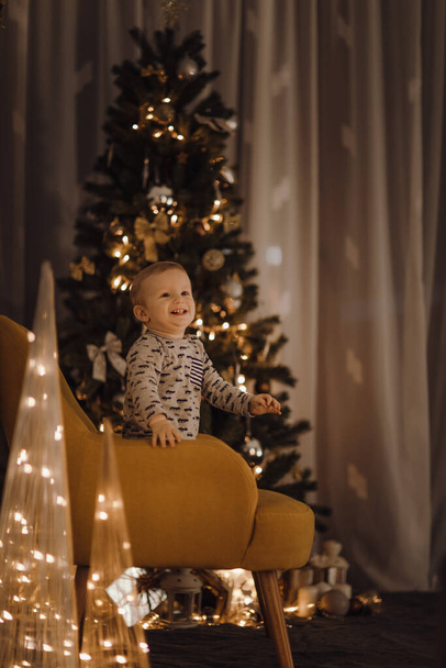 Mutlu çocuk arka planda Noel ağacı ve süslemeleri olan bir koltukta oturuyor.. - Fotoğraf, Görsel