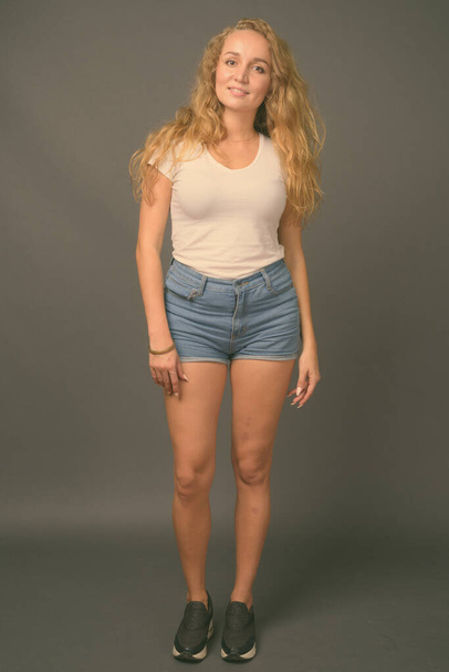 Jonge mooie vrouw met lange golvende blonde haren tegen grijze achtergrond - Foto, afbeelding