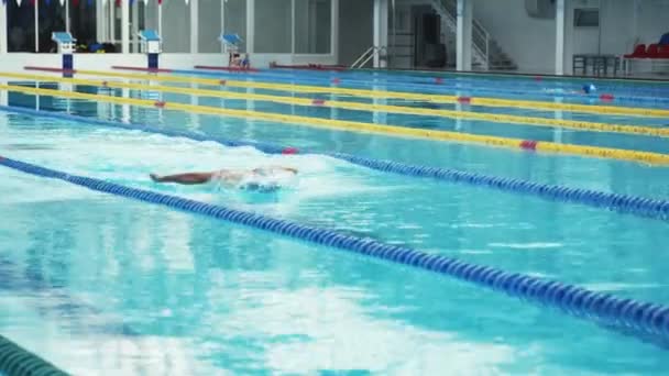 Nadador mal trabalhando na piscina interior nadando através da pista. - Filmagem, Vídeo