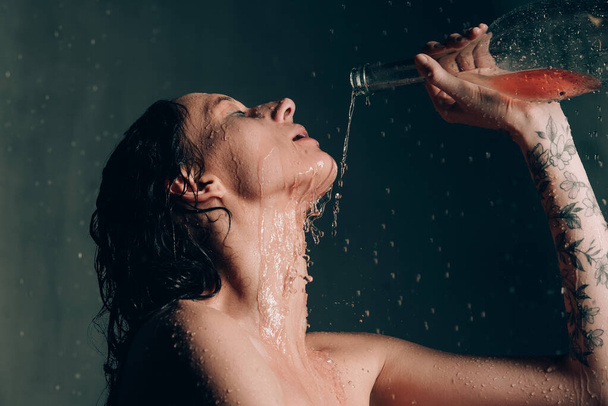 若いかわいいブルネットの女性は、水と花とお風呂で入れ墨。黒風呂で珍しい写真撮影中の裸のモデルワインを飲む - 写真・画像