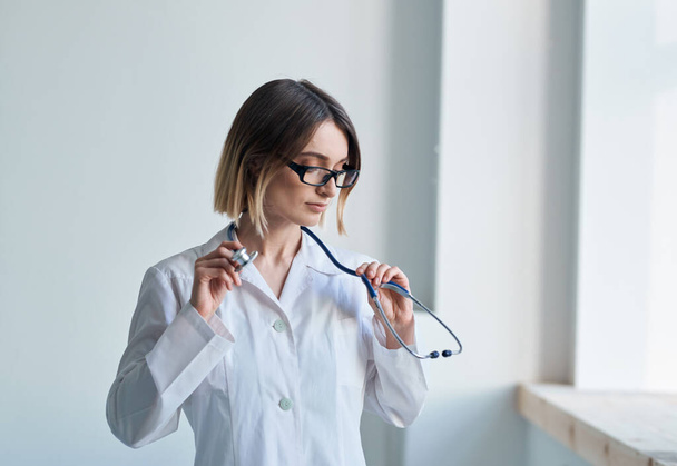 Professional doctor woman stands near the window and a stethoscope around her neck - Zdjęcie, obraz