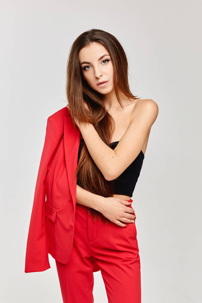 Slim model girl with long hair and perfect makeup in red stylish outfit posing at the grey background, isolated - Φωτογραφία, εικόνα