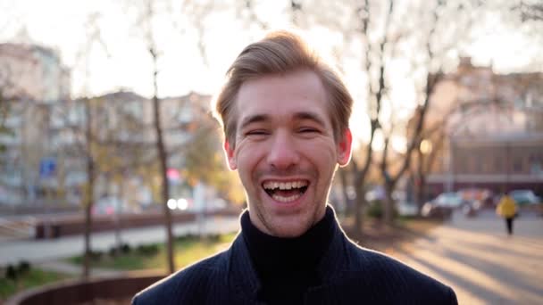Πορτρέτο. Ευτυχισμένος Ευρωπαίος γελάει περίεργα στο φόντο του αστικού ηλιοβασιλέματος. Συναισθηματικά - Πλάνα, βίντεο
