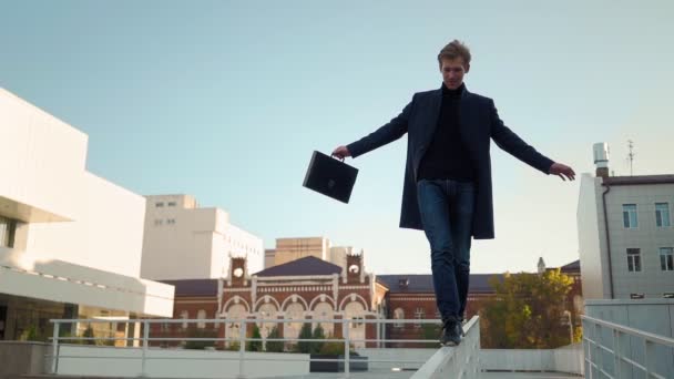 Παιχνιδιάρης ευτυχισμένος άνθρωπος με επιχειρηματικό χαρτοφύλακα με τα πόδια κατά μήκος κιγκλίδωμα και πιάνει την ισορροπία - Πλάνα, βίντεο