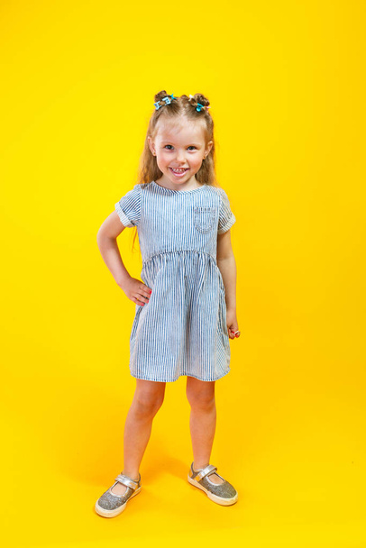 Adorable little girl in trendy dress posing against yellow background - Фото, изображение