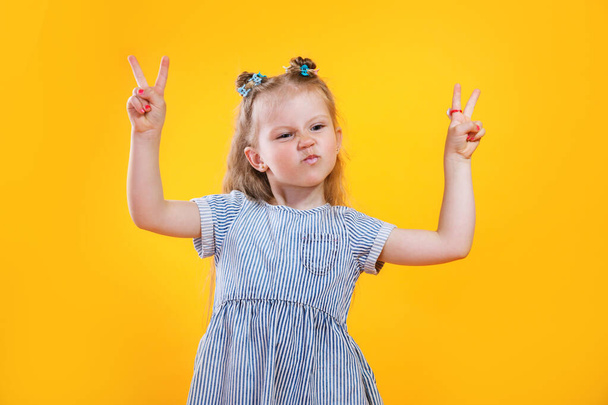 Funny little girl showing peace gesture on yellow background.. - Foto, imagen