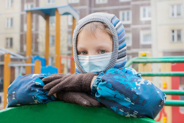 Portrait of a preschool boy on the playground wearing a mask and autumn clothes, children in quarantine, coronavirus pandemic, virus protection, isolation and social distance with covid 19 - Zdjęcie, obraz