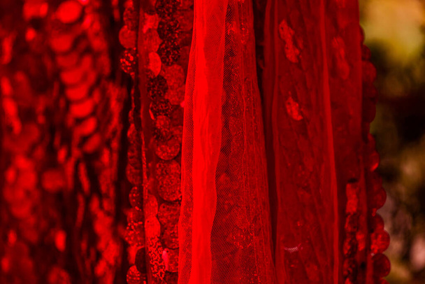 Czerwone cekiny. Błyszczące cekiny w tle. Czerwony cekinowy materiał na tło. prostokątny czerwony błyszczący materiał z cekinami, tło świąteczne. Sekweny na tkaninie, czerwone koraliki. Materiał modowy - Zdjęcie, obraz