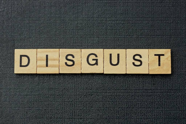 gray word disgust from small wooden letters on a black table - Photo, Image