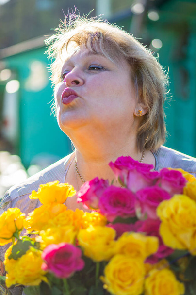 Χαρούμενη ώριμη γυναίκα με λουλούδια ξεκουράζεται σε ένα πάρκο της πόλης  - Φωτογραφία, εικόνα