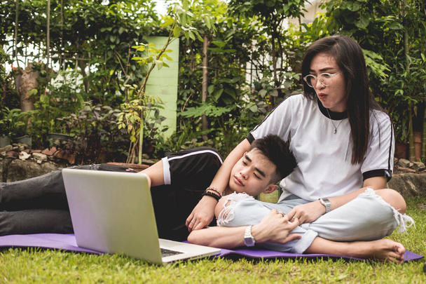 Un adolescent asiatique couple obligations sur une revue sur l'ordinateur portable pour un examen en ligne. Allongé sur un tapis à la cour de la maison. - Photo, image
