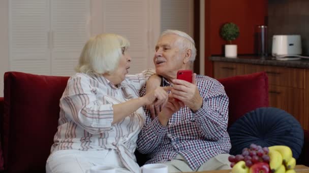Ηλικιωμένοι παππούδες μιλάνε και χρησιμοποιούν υπολογιστή κινητού τηλεφώνου στο σπίτι. Αγορές Διαδικτύου - Πλάνα, βίντεο
