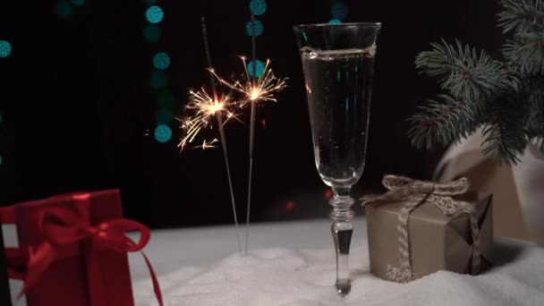 een glas champagne staat in de sneeuw, twee sterretjes branden naast elkaar - Video