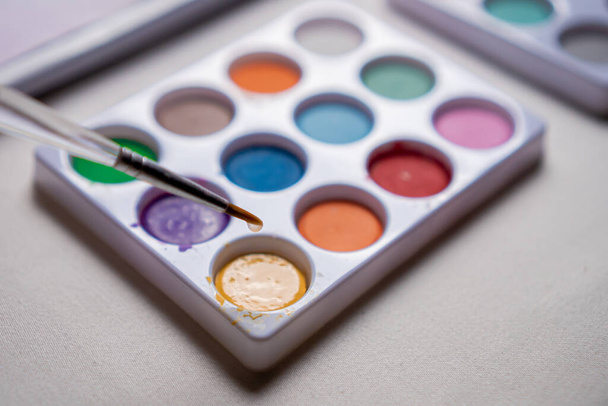 Acuarelas de colores en una mesa blanca y hasta un pincel con goteo de agua en las pinturas en primer plano concepto. - Foto, imagen