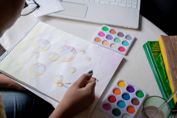 Dibujo de burbuja para colorear a mano femenina con acuarelas de colores en un cuaderno de bocetos sobre una mesa blanca. - Foto, imagen