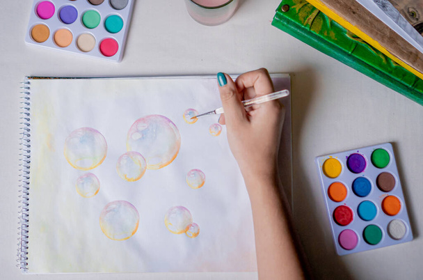 Vrouwelijke hand kleuring bel tekening met gekleurde aquarellen in een schetsboek op een witte tafel. - Foto, afbeelding
