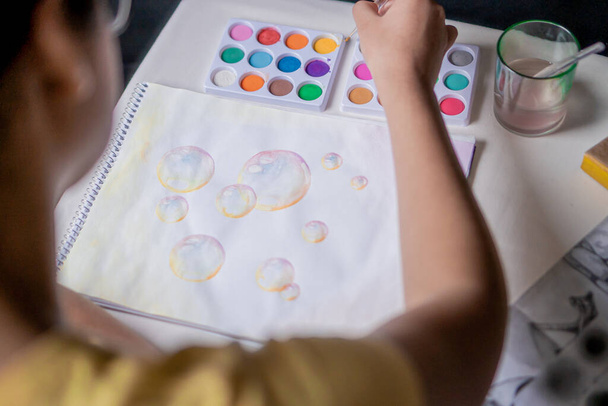 Mulher pintura colorido bolha desenho em um caderno de esboços com aquarelas coloridas em uma mesa branca. - Foto, Imagem