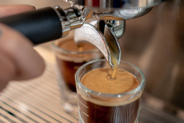 Γκρι καφετιέρα με δύο μικρά γυάλινα φλιτζάνια γεμάτα με καφέ σε μεταλλικό πλέγμα σε κοντινή απόσταση. - Φωτογραφία, εικόνα
